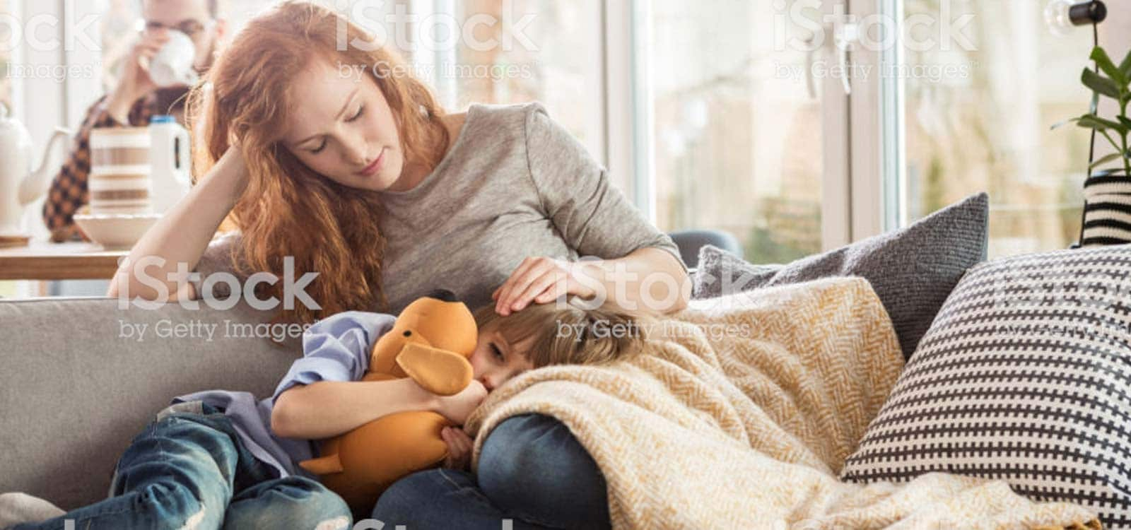 Young woman with ill young child sitting on couch